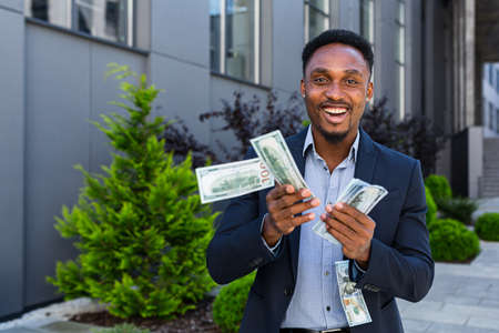 Happy successful African American businessman counts, waves, throws, show off, flaunt, cash money background a modern office building looking at camera Celebrate Winner success in betting stock marketの写真素材