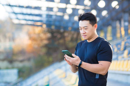 A healthy man watches a video on a mobile phone after a workout while sitting outdoors using an app on a 4g wireless device. Asian athlete is happy and smiling after running restの写真素材
