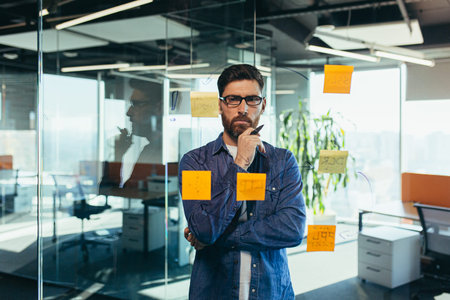 Young bearded executive manager businessman CEO writes his strategy ideas on notes on a blackboard,...