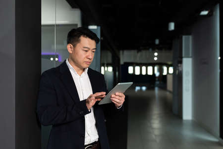 Serious asian male worker focused on work working with tablet computer in modern officeの写真素材