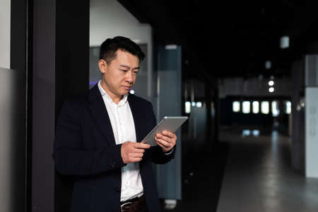 Serious asian male worker focused on work working with tablet computer in modern officeの写真素材