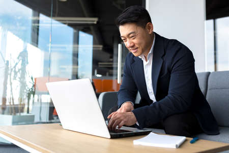 Successful and happy asian man working online remotely on laptop smiling happy with plan and taskの写真素材