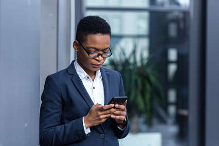 thinking business woman using phone, african american woman in business suit near office concentratedの写真素材
