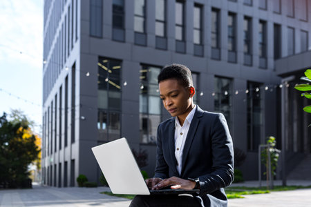 Young serious african american woman studying online sitting remotely in the park, businesswoman...