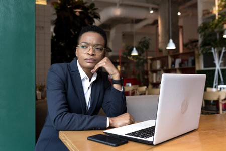 Young business woman working is a cafe with a laptop, African-American is focused on the end of the...