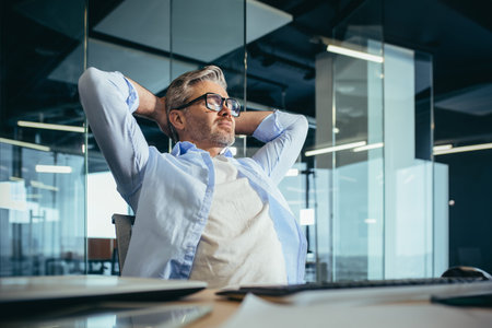 pensive and dreamy experienced businessman owner boss, sitting at work, throwing his hands behind his head, restingの写真素材