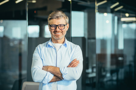 Portrait of senior and experienced male boss boss, with arms crossed, smiling and looking at camera,...