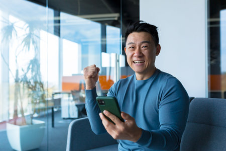 Successful and happy asian businessman man celebrating victory sitting and working in modern office...