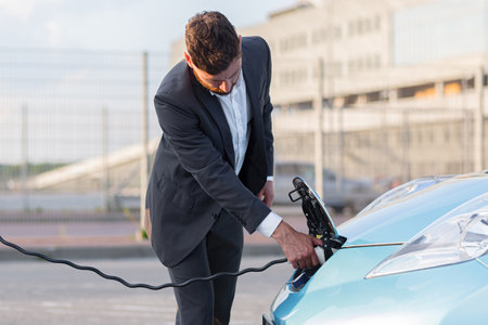 A man at a gas station charges an electric car, a businessman connects a charger to a carの写真素材