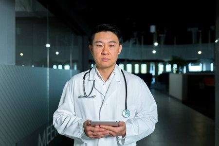 Concentrated and confident, Asian doctor, in the corridor of the clinic, looks at the camera and...