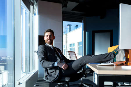 Satisfied businessman, happy and resting, man threw his feet on the table, and dreams of successful projectsの写真素材