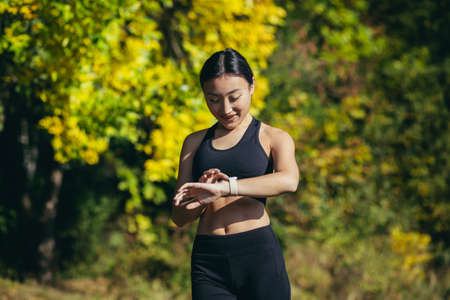 Portrait of young fitness woman athlete, asian looking at camera and smiling, enjoying fitness smart watch, for fitnessの写真素材