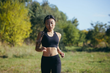 Beautiful Asian woman running in the morning in the park, a woman dressed in a dark sports suit