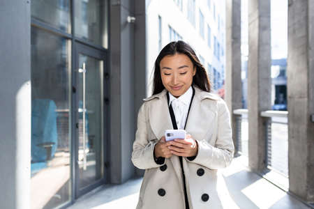 Young beautiful asian woman texting on the phone, chinese student on campus, walking after schoolの写真素材
