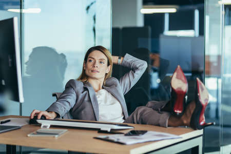 Woman director resting and dreaming at work, business woman throwing her hands behind her head and feet on the table, resting on the day at workの写真素材