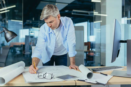 An experienced architect working on a drawing, a man in a modern office at the computer, a designer draws a modern projectの写真素材