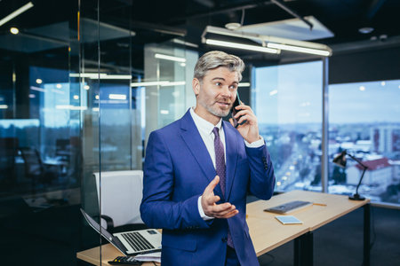Successful boss working in a modern office, gray-haired businessman talking on the phoneの写真素材