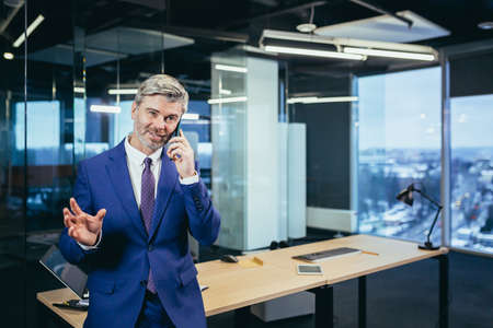 Successful boss working in a modern office, gray-haired businessman talking on the phoneの写真素材
