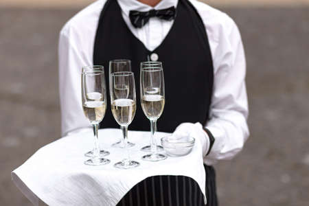 Close-up photo of glasses with champagne, waiter holding drinks on a trayの写真素材