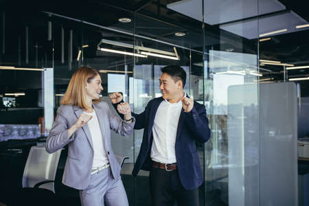 Two business people celebrating a successful deal, dancing in the office, Asian man and blonde womanの写真素材