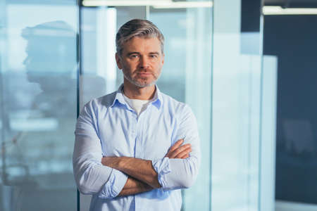 Concentrated and serious boss looking at camera with arms crossed, businessman in modern officeの写真素材