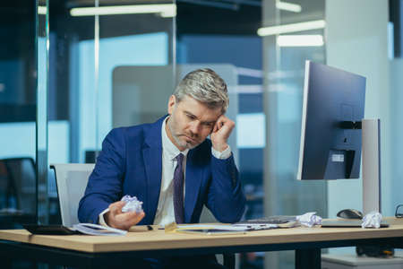 The businessman works at the computer, bored me and paper and documentsの写真素材