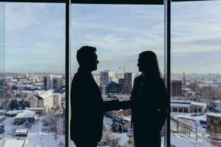 Silhouettes of two employees team of businessmen, Asian man and woman are consulting and communicating, working in a modern office by the windowの写真素材