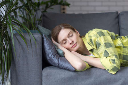 Close-up photo of tired woman sleeping with closed eyes on sofaの写真素材