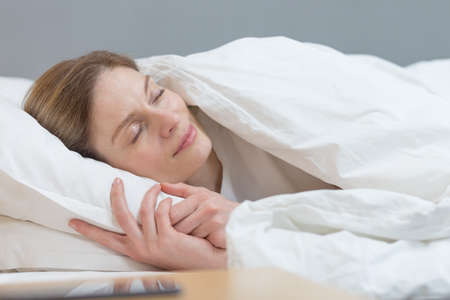 Close-up photo of a woman sleeping under a blanket smiling in a dreamの写真素材