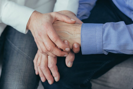 close up older elderly people hands. Old man holds a woman hand sitting together at home indoor....