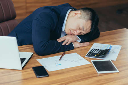 Tired young asian man businessman, worker. Lawyer fell asleep on his hands on the desk at work in the officeの写真素材