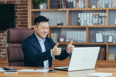 Young handsome asian man, businessman, lawyer, director talking on a video call from a laptop in the office, holds a meeting, consultation, discussionの写真素材