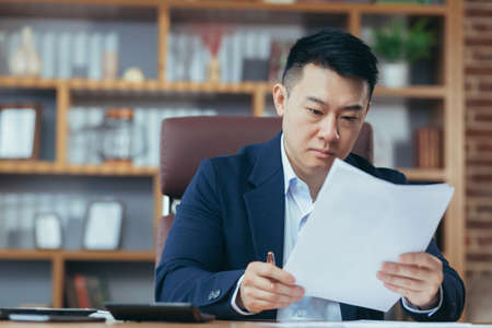Portrait of young handsome asian businessman, director working with documents in office, serious, looking at cameraの写真素材