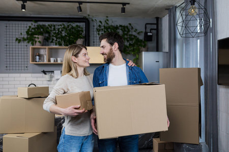 Happy couple man and woman live together, moved to a new rented apartment, holding cardboard boxes
