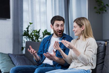 Happy couple man and woman on the couch sitting and rejoicing in a positive pregnancy test
