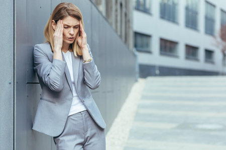 Business woman near office building outside, has severe headache, tired and depressed holding hands behind headの写真素材