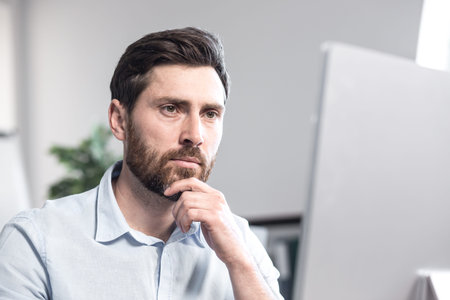 Portrait of an office worker. Thoughtful, serious, with a bear. Sitting at a desk in the office at...