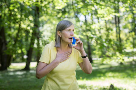 Senior retired woman with asthma breathing in an inhaler in a summer parkの写真素材