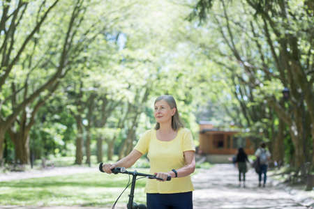 Retired woman resting in the park, gray-haired Persian woman walks with a bicycle on a summer dayの写真素材