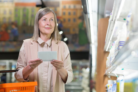 Senior woman in the store chooses goods in the dairy department near the refrigeratorsの写真素材