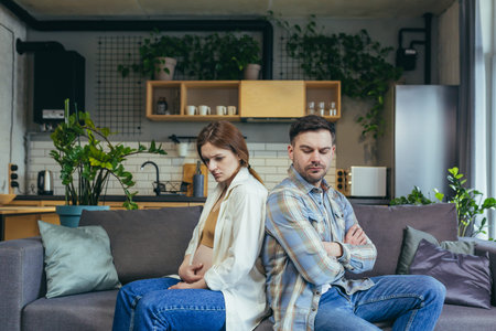 family conflict. Young couple, pregnant woman and man sitting on sofa at home with their backs to...
