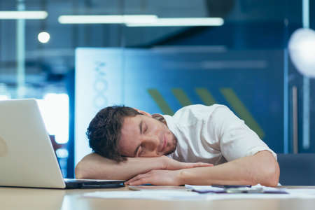 Young tired businessman sleeping on the desk at workplace in the officeの写真素材