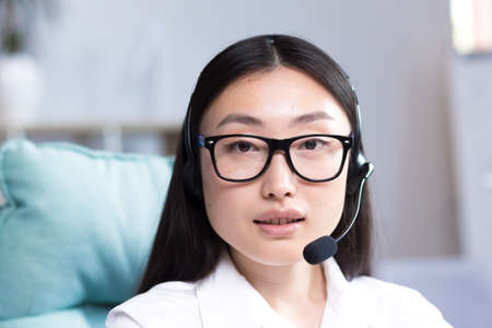Close-up portrait of a young beautiful asian woman with glasses smiling and looking at the camera, uses a headset for video communication call center employeeの写真素材
