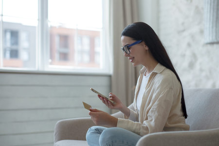 Young beautiful woman in glasses smiling and happy doing online shopping in online store sitting on...