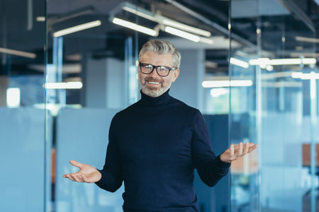 Senior gray-haired male businessman looking into web camera and smiling standing in office online...
