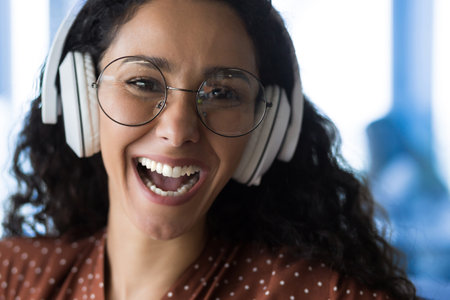 Close-up photo portrait of happy woman wearing glasses, smiling and happy listening to music in white headphones and looking at camera, selected focusの写真素材