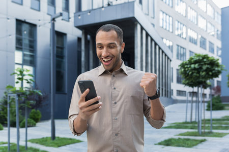 Successful african american businessman outside office building using smartphone, smiling and happy...