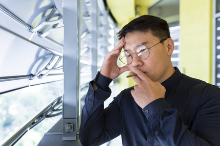 Asian businessman upset and sad in depression smoking cigarettes on balcony of office building, boss...