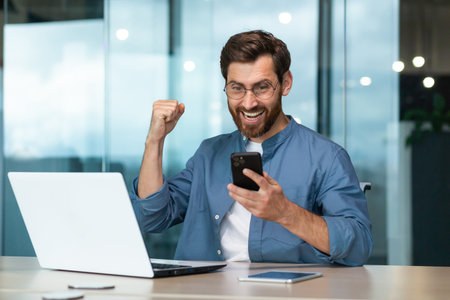 Businessman celebrating success and triumph, man in shirt working inside modern office with laptop...