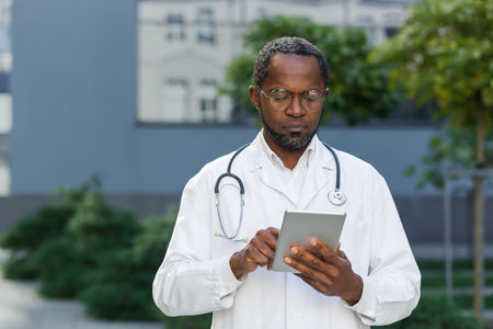 Portrait of serious and focused doctor at work, african american man in glasses working with tablet computer outside clinic.の写真素材